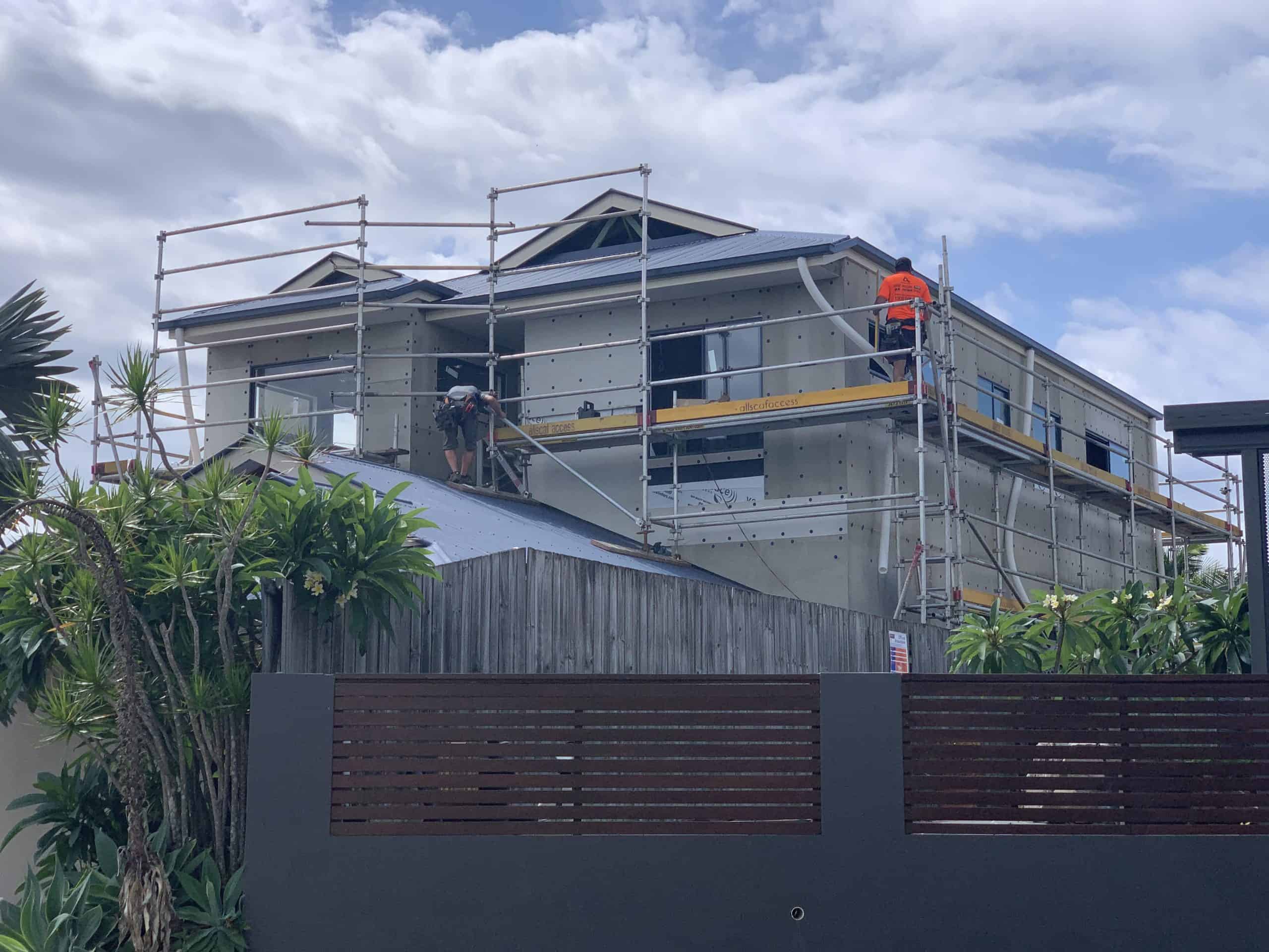 A home extension in progress, house is surrounded by scaffolding and two builders.